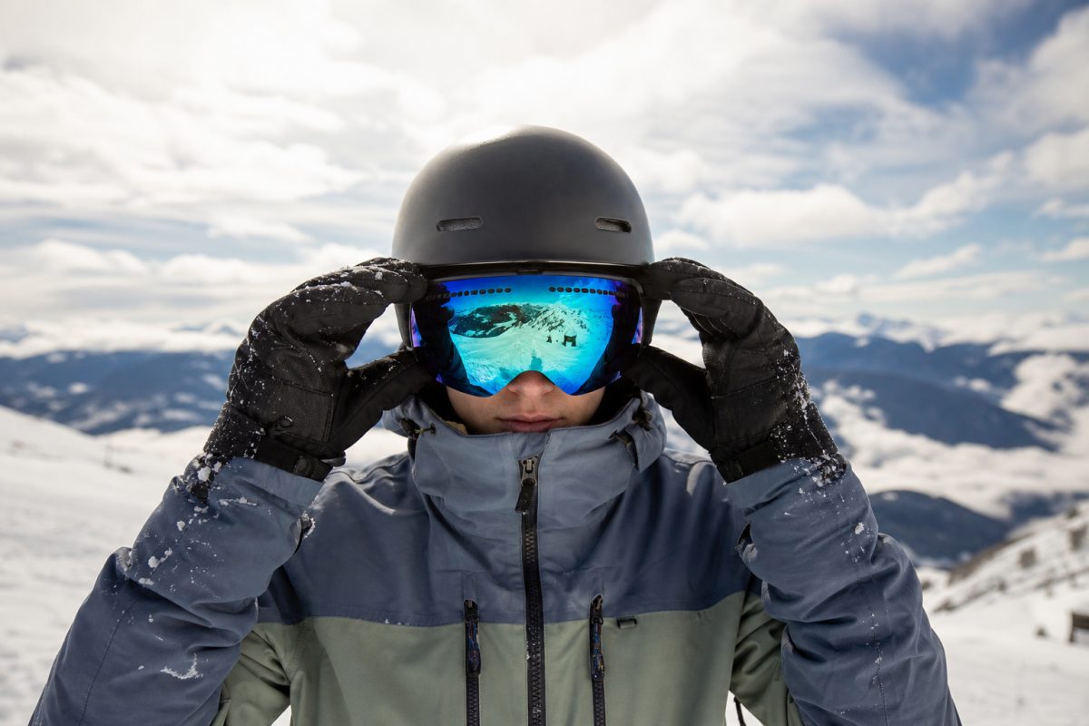 Snowboardos sportos síszemüveget igazít sisakkal havas pályán