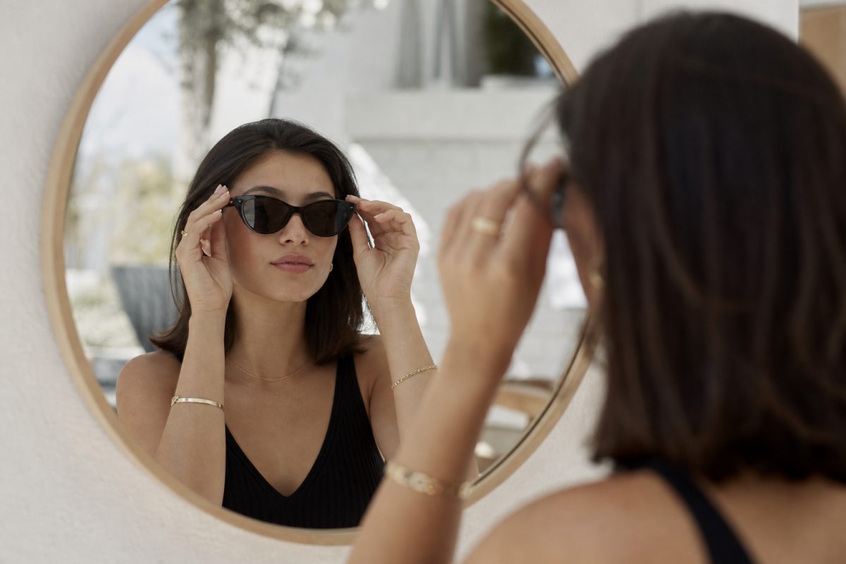 Fekete cat-eye napszemüveget próbáló nő tükör előtt
