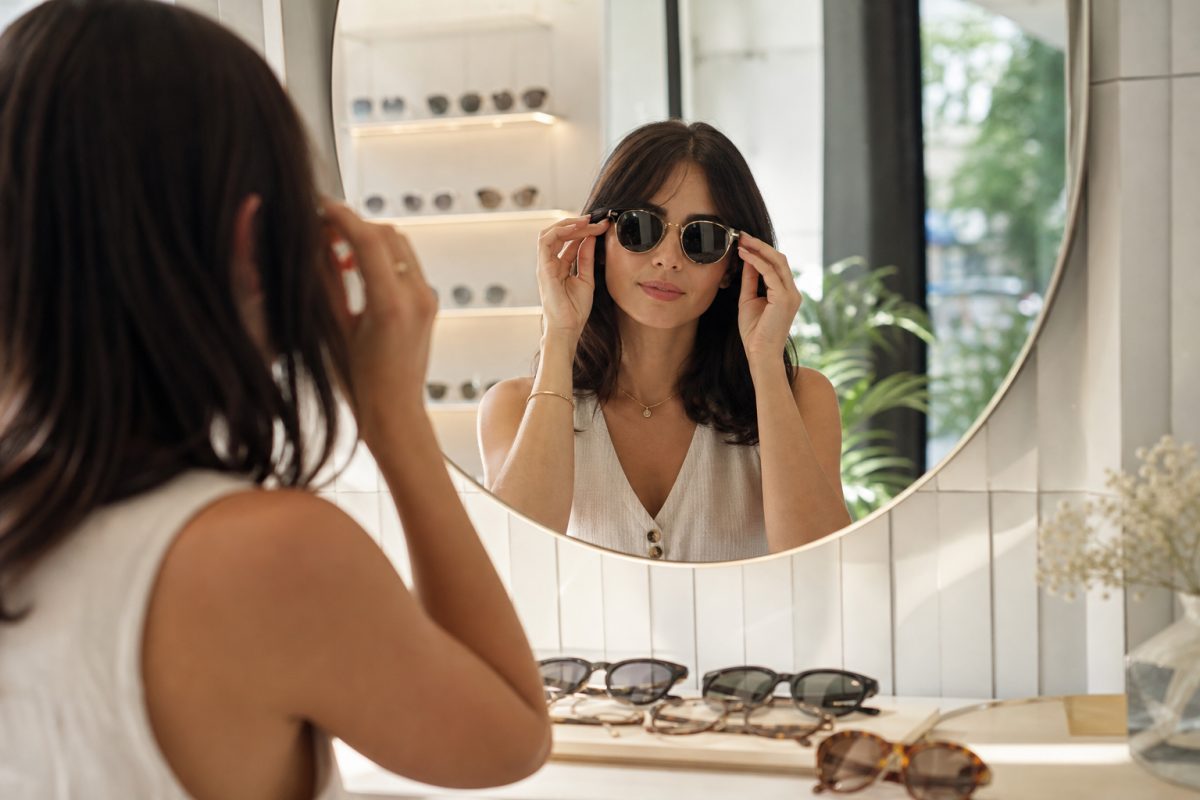 Nő különböző tiffany napszemüveg stílusú kereteket próbál tükör előtt